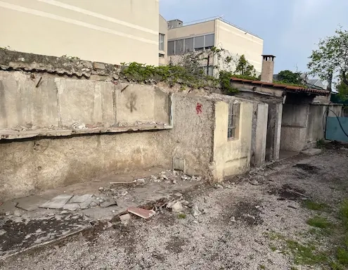 Mur en ruine avec gravats et végétation.