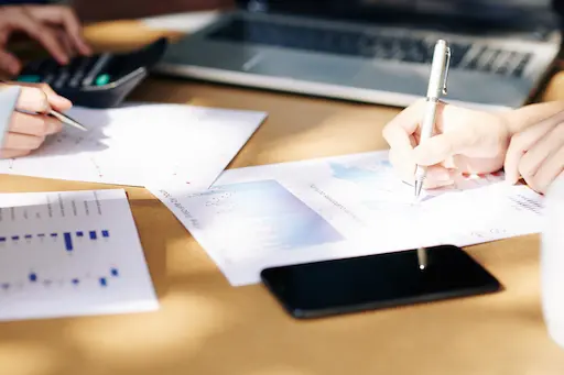vue sur des documents et des mains avec des stylos et un téléphone portable