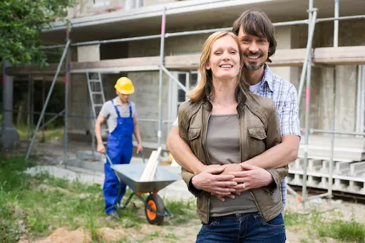 courtage pour construction neuve avec innova solution couple souriant devant une maison en construction et un ouvrier avec une brouette