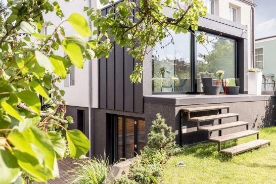 Maison moderne avec terrasse ensoleillée et jardin verdoyant.