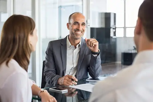 innova solution votre allié dans votre projet de construction homme souriant en costume assis à une table avec 2 personnes de dos