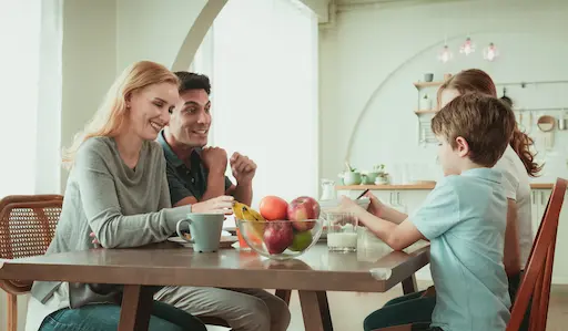 couple avec enfants assis à table avec un saladier de fruits