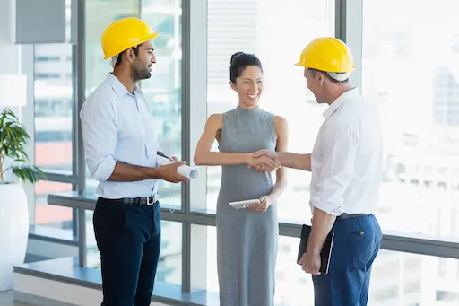 femme souriante serrant la main d'un homme avec un casque de chantier
