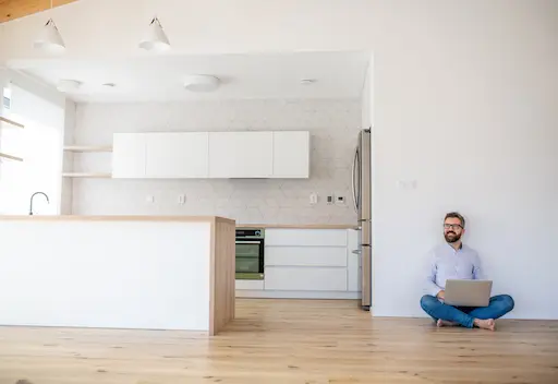 homme assis souriant au sol dans son appartement à côté de sa cuisine