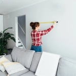 Femme mesurant un mur dans un salon moderne.