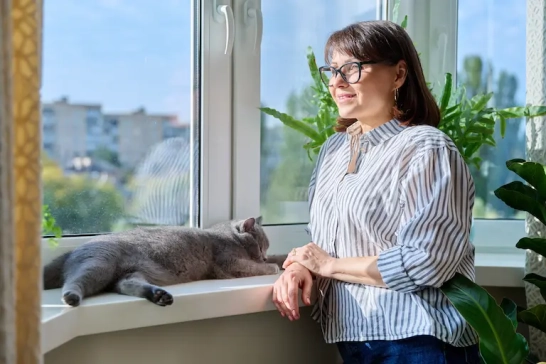 Femme souriante près d'un chat à la fenêtre.