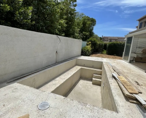 Marches et parois du bassin maçonné avant ses finitions, avec le jardin visible à l’arrière-plan.