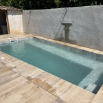 Piscine rectangulaire mise en eau, bordée d’une terrasse à l’aspect bois entre des murs maçonnés.